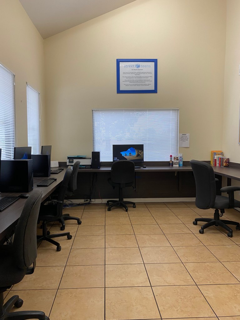 A quiet computer lab with multiple workstations and a 'Street Teens' framed notice on the wall.